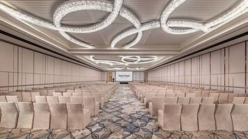 A spacious conference room with rows of chairs, a patterned carpet, and a large screen at the front.