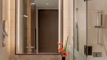 Un baño moderno con un espejo grande, cabina de ducha de vidrio, encimera de mármol y tocador de madera.