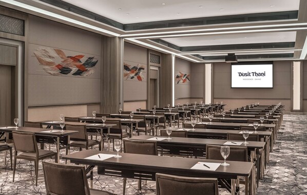 Un salón de conferencias con mesas y sillas, una pantalla grande que muestra 'Dusit Thani Residence - Davao' y arte abstracto en la pared.
