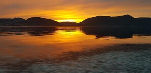 Ein ruhiger See mit Sonnenuntergang, dessen Spiegelung sich im Wasser zeigt, umgeben von Bergen.