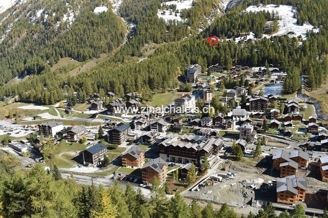 Vista aérea de un complejo turístico de montaña con varias edificaciones tipo chalé, caminos y zonas boscosas circundantes.