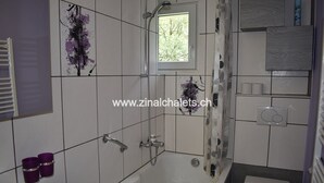 A bathroom with a bathtub, toilet, and a small window. - Appartment in a building in Zinal - 1 bedroom with 1 double bed (140x200) - 1 bedroom with 2 bunk be (Zinal)