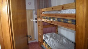 A bunk bed room with a wooden door, a window with curtains, and a radiator. - Appartment in a building in Zinal - 1 bedroom with 1 double bed (140x200) - 1 bedroom with 2 bunk be (Zinal)