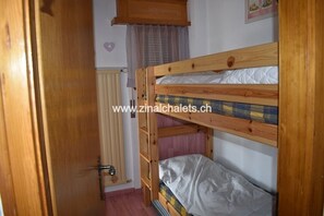 Habitación con literas, una puerta de madera, una ventana con cortinas y un radiador.