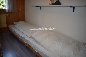 Una cama individual con colchón blanco y cabecera, apoyada en una pared de madera.