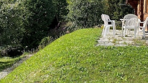 A grassy area with white plastic chairs and a table, surrounded by dense greenery and a stone pathway. - Individual chalet in Zinal - 1 bedroom with a double bed (140x200) - 1 bedroom with 2 beds - 1 bedro (Zinal)