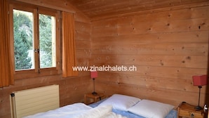 A wooden cabin room with a bed, two bedside tables, and a window. - Individual chalet in Zinal - 1 bedroom with a double bed (140x200) - 1 bedroom with 2 beds - 1 bedro (Zinal)