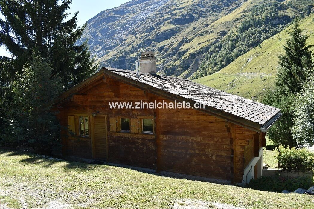 Una cabaña de madera con techo inclinado, rodeada de árboles y montañas.