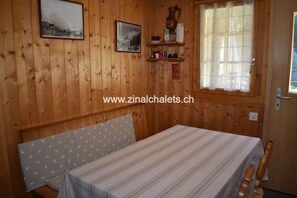 Una stanza in legno con un letto, una finestra con tende, uno scaffale con oggetti e due quadri appesi al muro.