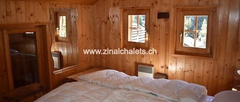 A wooden cabin room with a bed, two windows, and a small table.