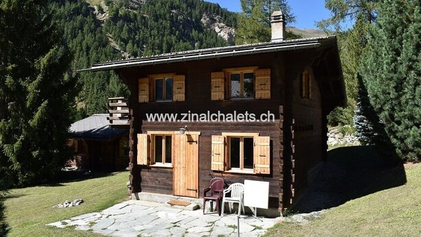 Un chalet en bois avec une adresse de site web, une terrasse en pierre et une chaise.