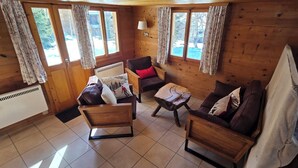 L’intérieur d’un chalet en bois accueillant, avec une cheminée, un canapé, un fauteuil et une petite table en bois.