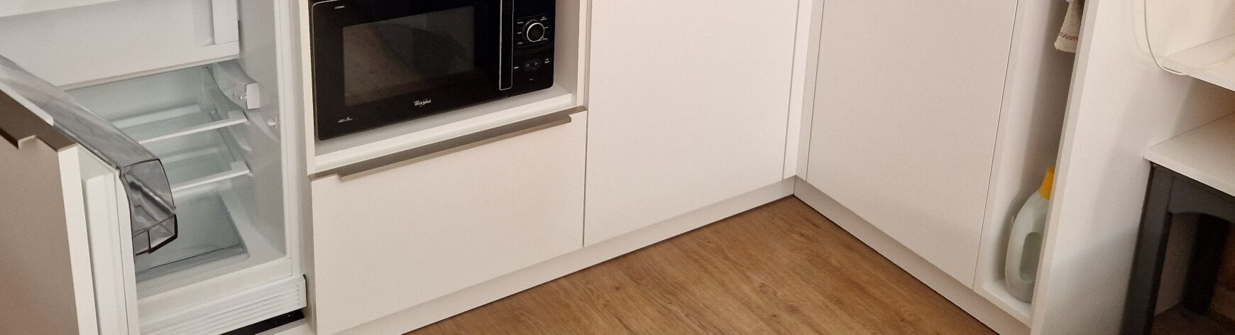 Een keuken met een magnetron, witte kasten en een houten vloer.