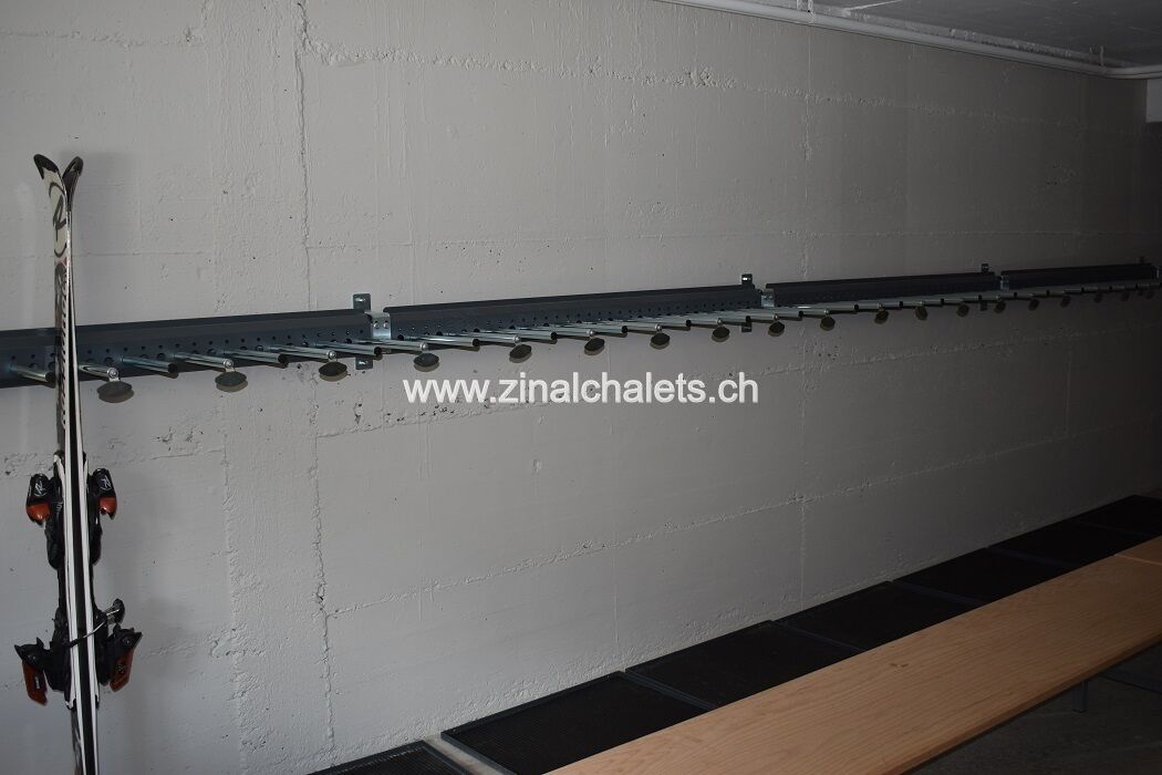 A ski rack with skis and poles against a white wall.