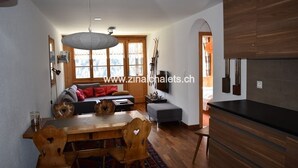 A modern kitchen with wooden cabinets, a dining table with chairs, and a large window with a view of the outdoors. - Appartment in a building in Zinal - 1 bedroom with 2 beds - 1 bedroom with 2 bunk beds - living room (Zinal)