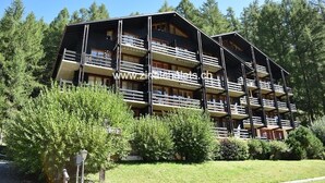 A multi-story building with balconies, surrounded by trees. - Appartment in a building in Zinal - 1 bedroom with 2 beds - 1 bedroom with 2 bunk beds - living room (Zinal)