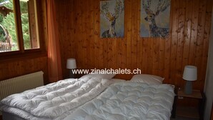 A wooden-paneled bedroom with a large bed, two bedside lamps, and two deer paintings on the wall. - Appartment in a chalet in Zinal - 2 bedrooms with 2 beds - living room - TV broadcasting - kitchen - (Zinal)