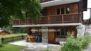 A two-story wooden chalet with a balcony, stone foundation, and a small outdoor seating area. - Appartment in a chalet in Zinal - 2 bedrooms with 2 beds - living room - TV broadcasting - kitchen - (Zinal)