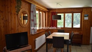 A wooden interior with a dining table, chairs, a TV, and a window with a view of trees. - Appartment in a chalet in Zinal - 2 bedrooms with 2 beds - living room - TV broadcasting - kitchen - (Zinal)