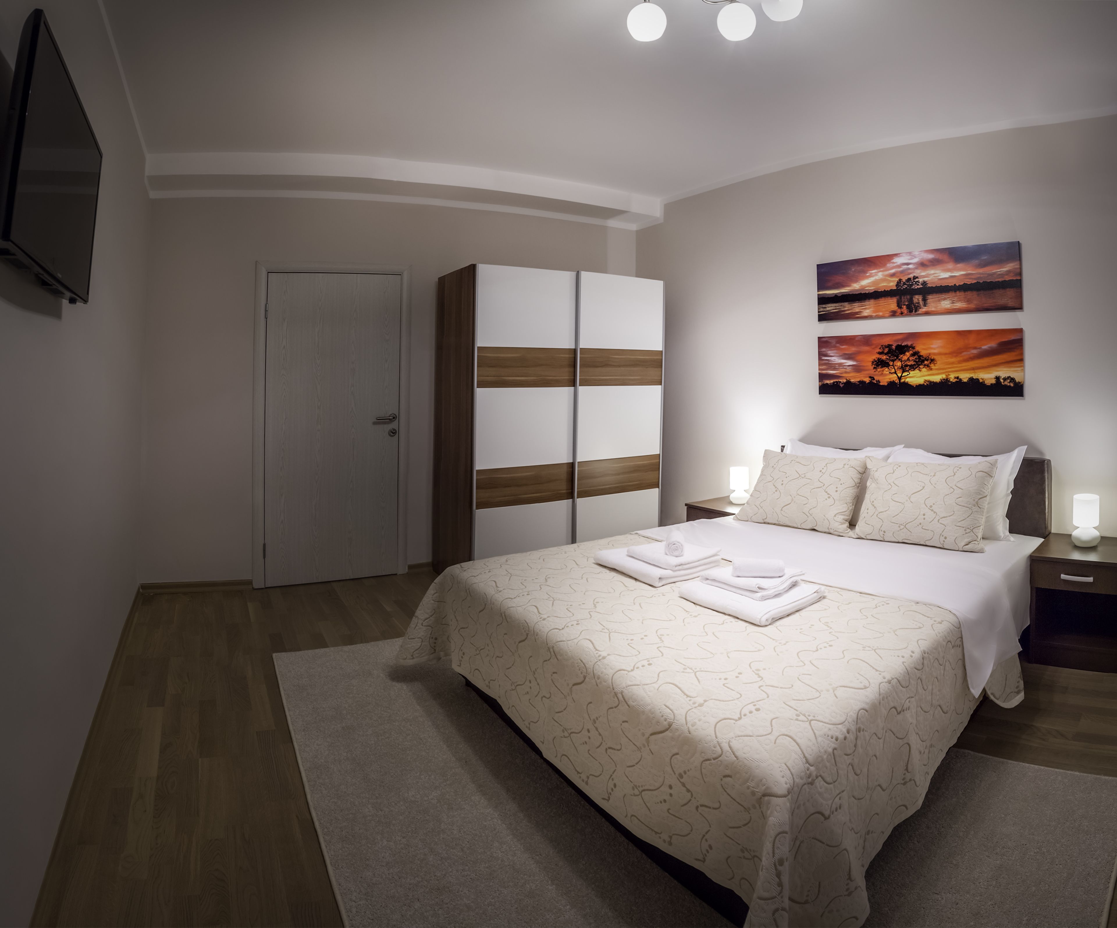 A bedroom with a bed, a wardrobe, a nightstand, and a painting on the wall.