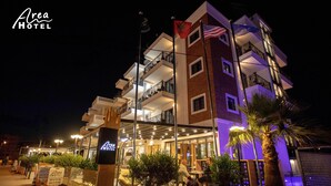 A multi-story hotel with balconies, outdoor seating, and a well-lit entrance. - Area Hotel (Ksamil)