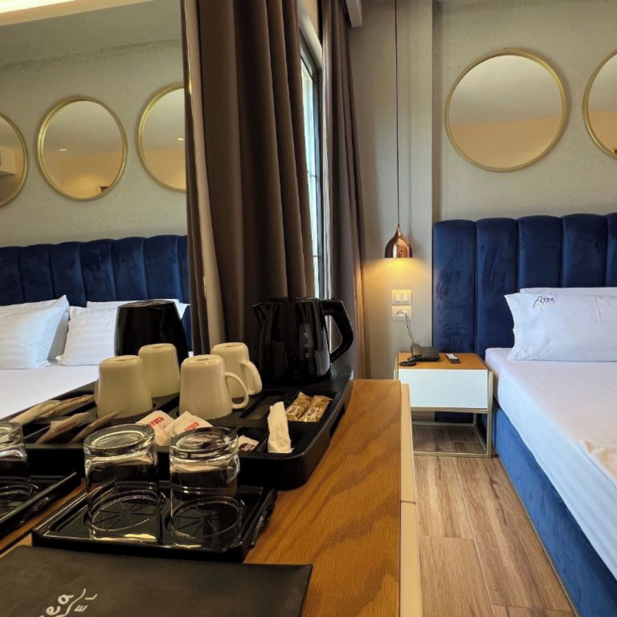 Ein Hotelzimmer mit zwei Betten, einem Esstisch mit Frühstücksgebäck und -spezialitäten, einer Kaffeemaschine und Nachttischlampen.