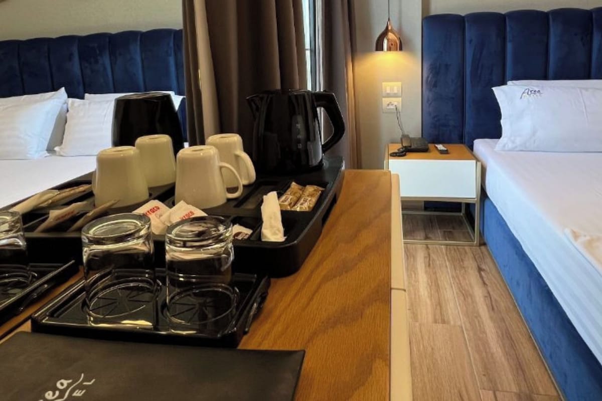 Ein Hotelzimmer mit zwei Betten, einem Esstisch mit Frühstücksgebäck und -spezialitäten, einer Kaffeemaschine und Nachttischlampen.
