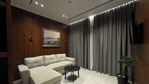 A modern living room with a sectional sofa, a small round coffee table, a potted plant, and a painting on the wall. - Area Hotel (Ksamil)