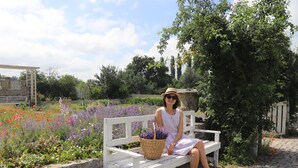 Una persona sentada en un banco blanco en un jardín con diversas flores y una cesta.
