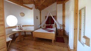 Un dormitorio con suelo de madera, una cama, una mesa redonda y una pared de ladrillo blanco.