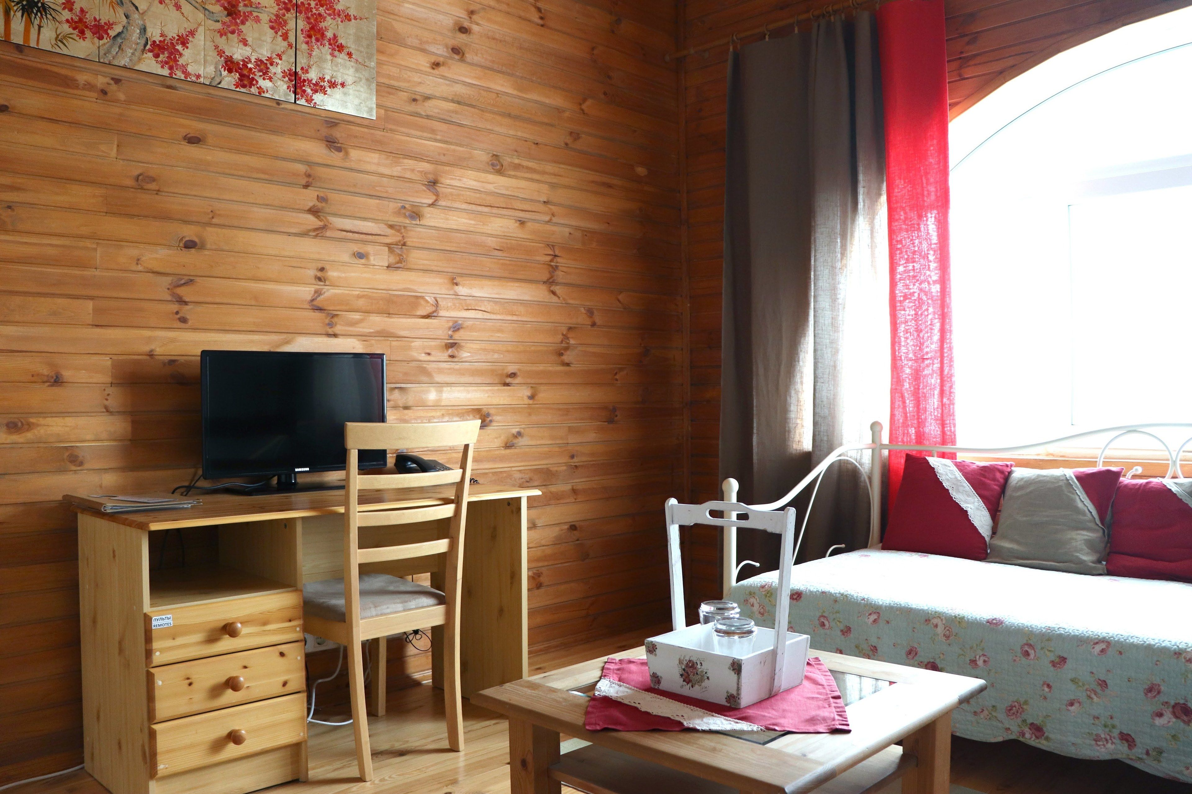 Una habitación de cabaña de madera con una cama, un escritorio con televisión, una silla y una mesita.