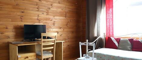 Una habitación de cabaña de madera con una cama, un escritorio con televisión, una silla y una mesita.