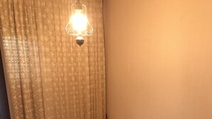 Quarto com duas cadeiras de madeira, estofadas com tecido floral, uma cortina estampada e um aplique na parede.