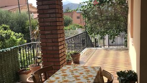 Uma área de pátio com toalha de mesa florida, parede de tijolos e plantas em vasos.
