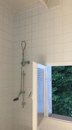 Un baño con ducha, ventana con vistas a la vegetación y pared de azulejos.