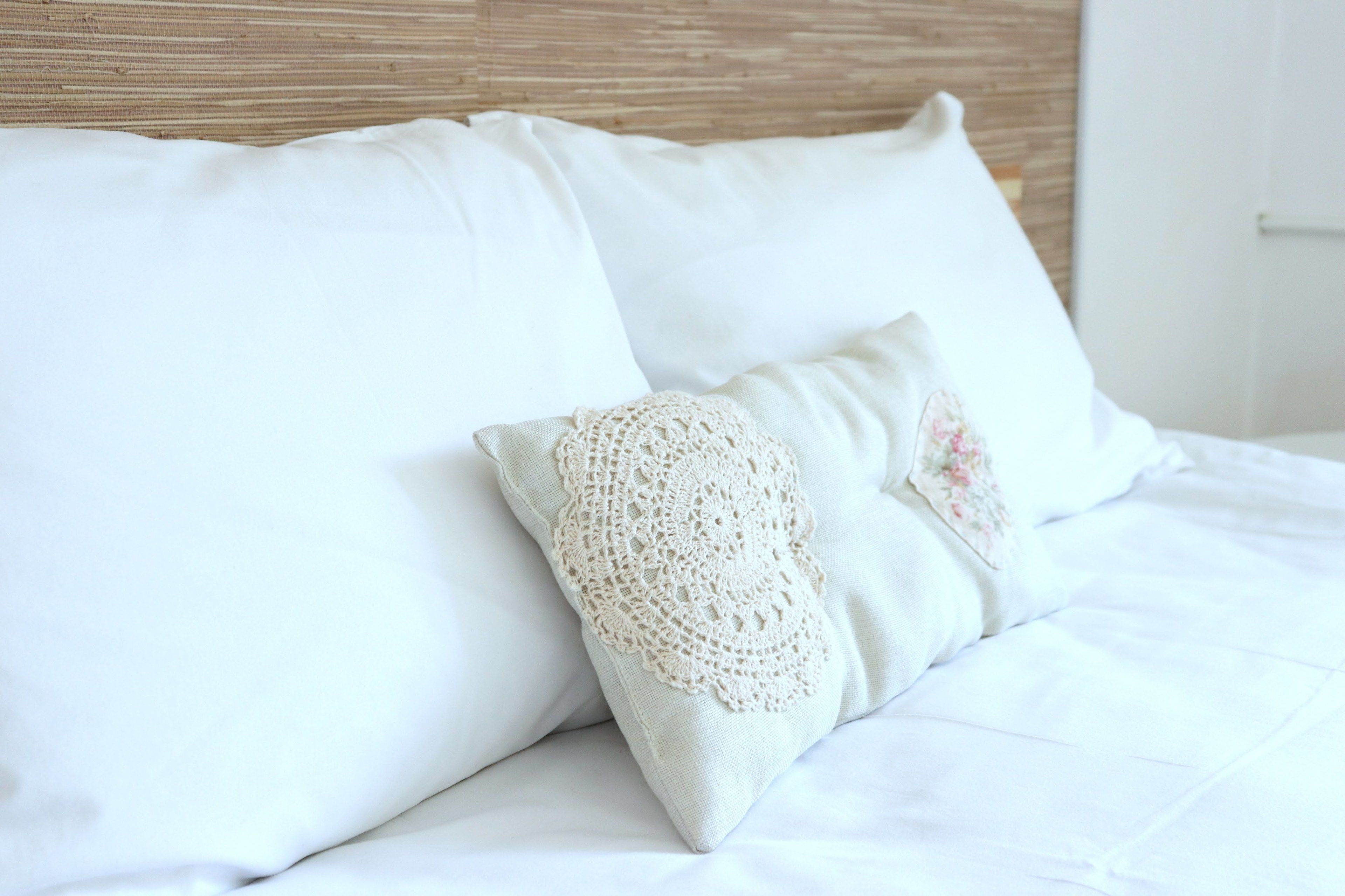 A bed with white bedding and two pillows, one with a crocheted cover and another with a floral design.
