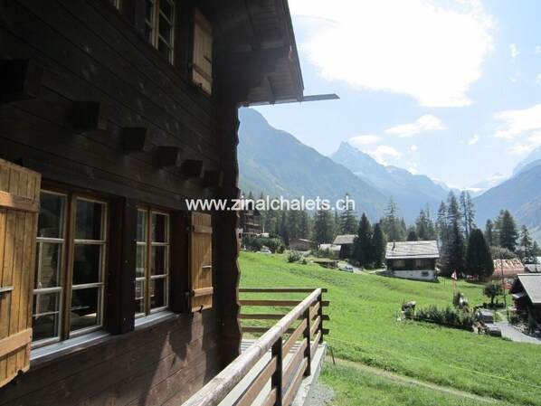 A wooden building with large windows and a balcony overlooking a green valley and mountains.