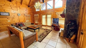 A log cabin interior with a wooden sofa, coffee table, and a television in the living area. - Spacious 5BR Mountain Lodge | Hot Tub, Pool Table & Scenic Views (Grassy Creek)