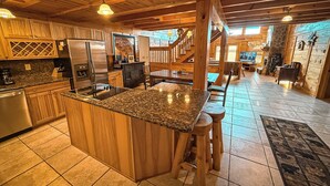 A spacious kitchen with granite countertops, wooden cabinets, and a central island with stools. - Spacious 5BR Mountain Lodge | Hot Tub, Pool Table & Scenic Views (Grassy Creek)