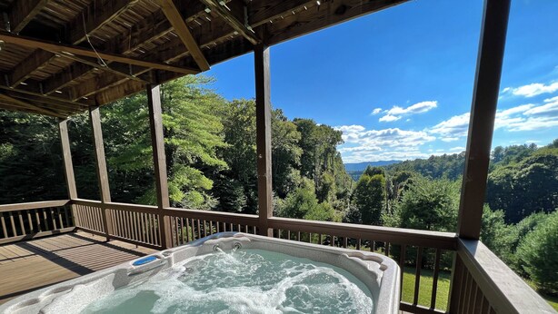 A hot tub on a wooden deck with a scenic view of a forest and mountains. - Spacious 5BR Mountain Lodge | Hot Tub, Pool Table & Scenic Views (Grassy Creek)
