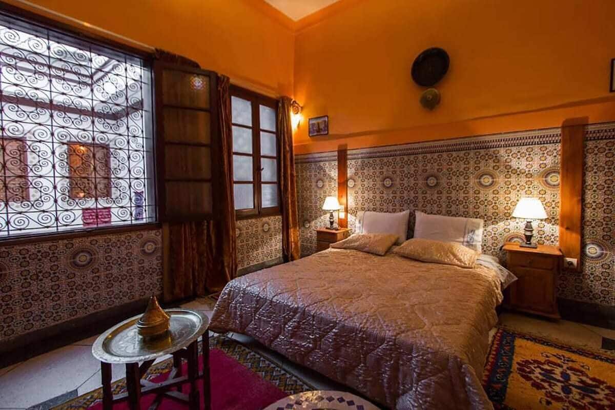 Une chambre de style marocain traditionnel, avec un grand lit, des murs à motifs et une fenêtre décorative.