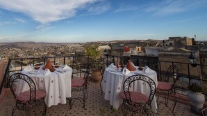 Terraza en la azotea con dos mesas dispuestas para comer, con vistas a un paisaje urbano.