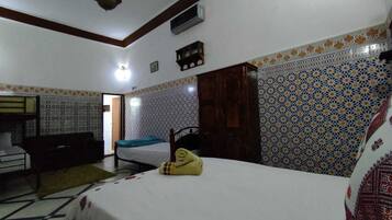 A bedroom with a bed, a wooden wardrobe, a desk, and patterned walls.