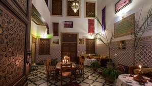 Un interior marroquí tradicional con un comedor, un sofá y elementos decorativos como un candelabro y tapices.