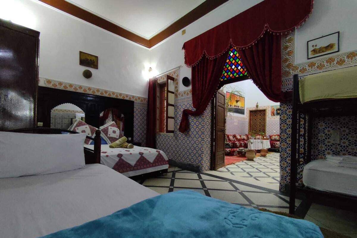 Une chambre d’hôtel avec deux lits, un mur décoré de motifs, un sol carrelé et une vue sur la cour.