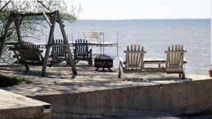 Una terraza de hormigón con sillas Adirondack y un columpio, con vistas a un cuerpo de agua.