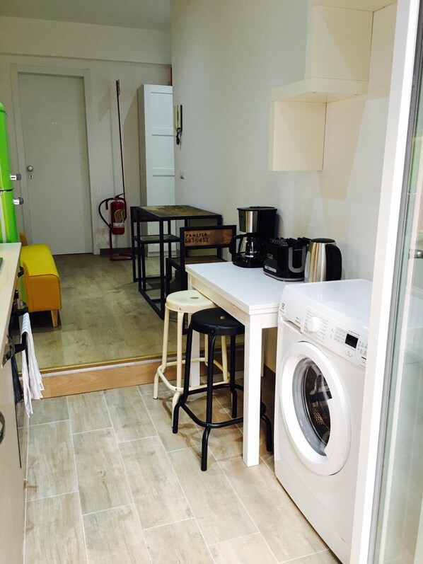 A compact kitchen with a washing machine, a coffee maker, and a fire extinguisher.