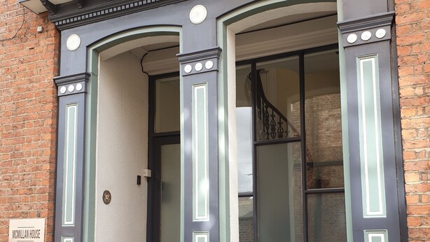 A brick building with a dark blue door and a sign reading "McMillan House." - McMillan House Studio Apartments (York)