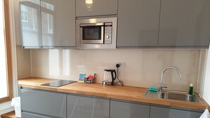 A modern kitchen with grey cabinets, a wooden countertop, a built-in microwave, a kettle, and a sink. - McMillan House Studio Apartments (York)