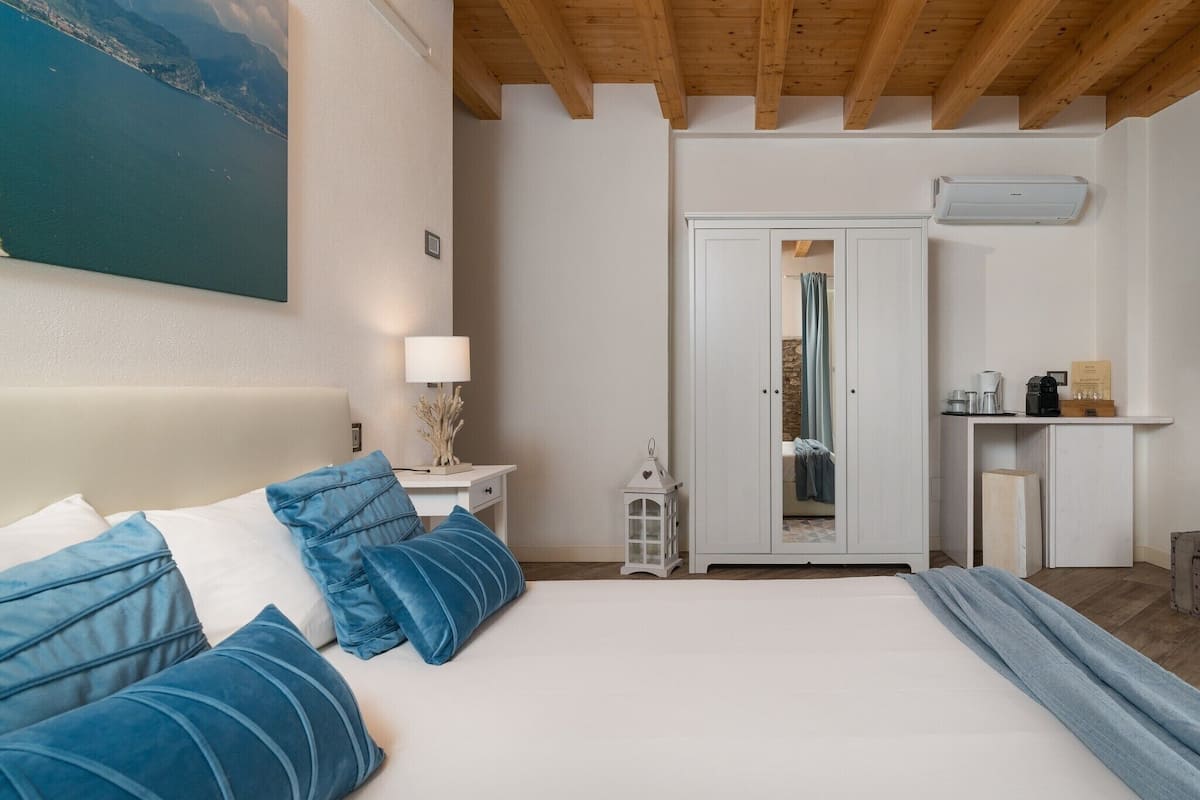 A bedroom with a bed, a nightstand, a lamp, a wardrobe, and a view of the sea.